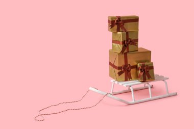 Pembe arka planda hediye kutularıyla kızak.
