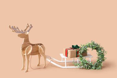 Hediye kutulu beyaz kızak, Noel çelengi ve bej arka planda tahta geyik.