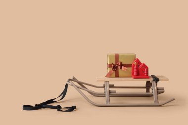 Noel hediyesi kutusu ve bej arka planda ev şeklindeki fenerle kızak.