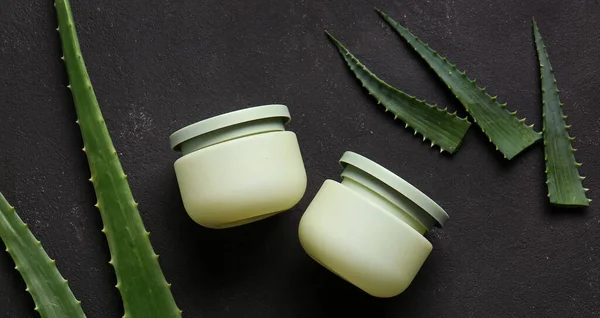 Siyah arka planda aloe vera yapraklı kozmetik kremi kavanozları.
