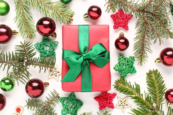Noel toplarıyla hediye kutusu, köknar ağacı dalları ve beyaz arka planda dekoratif yıldızlar.