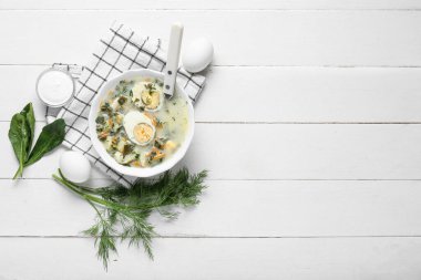 Beyaz ahşap arka planda ıspanak yapraklı, yumurtalı, dereotlu ve ekşi kremalı sebze çorbası.