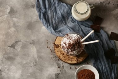 Krem şantili bir bardak soğuk kakao ve gri arka planda bir sürahi taze süt.