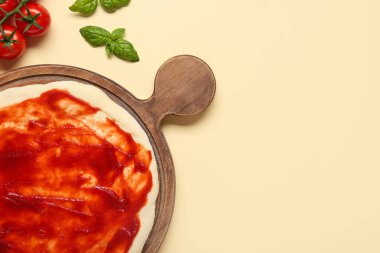 Lezzetli soslu pizza hamuru, domates ve bej arka planda fesleğen yaprakları.