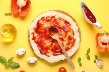 Lezzetli domates soslu pizza hamuru ve sarı arka planda malzemeler.