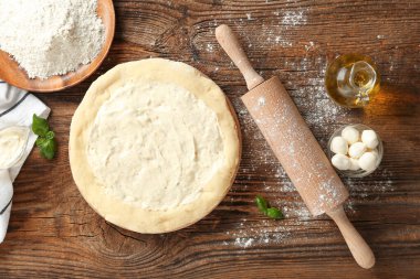 Lezzetli soslu pizza hamuru, mozarella topları, ahşap arka planda bir sürahi yağ ve un.