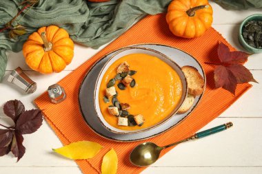 Bir kase lezzetli balkabağı kremalı çorba, tohumlu, kıtır kıtır ve sonbahar yapraklı beyaz ahşap arka plan