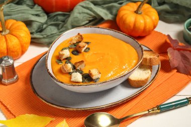 Bir kase lezzetli balkabağı kremalı çorba, tohumlu, kıtır kıtır ve sonbahar yapraklı beyaz ahşap arka plan