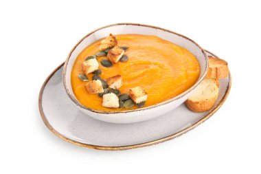 Beyaz arka planda çekirdekli ve kızarmış ekmekli bir kase lezzetli kabak kremalı çorba.