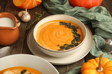 Bir kase lezzetli kabak kremalı çorba, tohumlu kekik ve ahşap zemin üzerinde sarımsak.