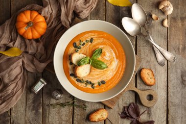 Bir kase lezzetli balkabağı kremalı çorba içinde tohumlar, kızarmış ekmekler, fesleğenler ve ahşap arka planda kekik filizleri.