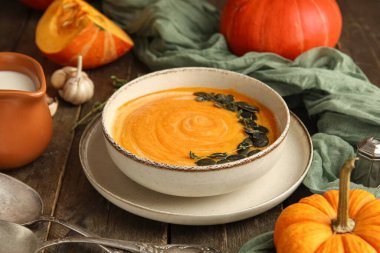 Bir kase lezzetli kabak kremalı çorba, tohumlu kekik ve ahşap zemin üzerinde sarımsak.