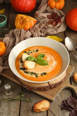 Bir kase lezzetli balkabağı kremalı çorba içinde tohumlar, kızarmış ekmekler, fesleğenler ve ahşap arka planda kekik filizleri.