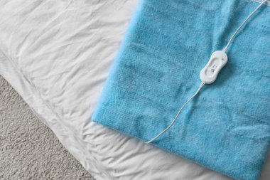 Yatak odasındaki battaniyenin üzerine katlanmış elektrikli ısıtma yastığı.