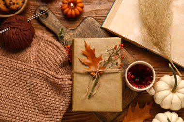 Kahverengi ahşap arka planda çay, örgü ipliği, süveter ve sonbahar süslemeleri olan kitaplar.