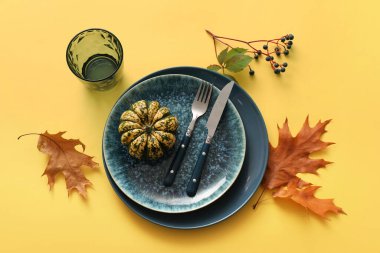 Sarı arka planda balkabağı ve sonbahar yapraklarıyla güzel bir masa.