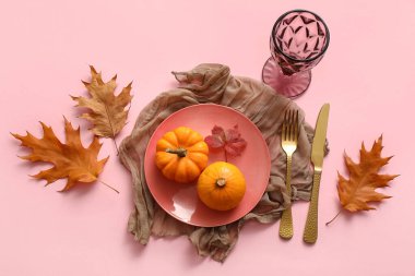 Pembe arka planda balkabakları ve sonbahar yapraklarıyla güzel bir masa.