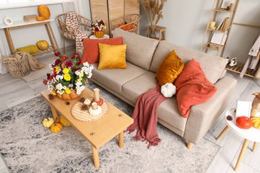 Rahat kanepe, masalar, balkabakları ve güzel sonbahar çiçekleri oturma odasının içinde.