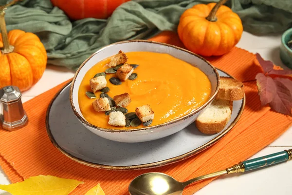 Bir kase lezzetli balkabağı kremalı çorba, tohumlu, kıtır kıtır ve sonbahar yapraklı beyaz ahşap arka plan