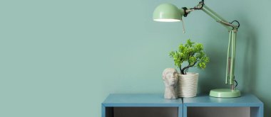 Açık mavi duvarın yanındaki rafta bitki ve dekor bulunan lamba. Tasarım için pankart