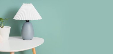 Açık mavi duvarın yanındaki masada bitkisi olan şık bir lamba. Tasarım için pankart