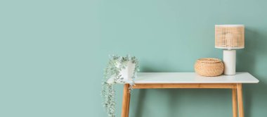 Sepetli şık bir lamba ve açık mavi duvarın yanındaki masada bitki. Tasarım için pankart