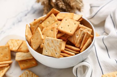 Beyaz arka planda lezzetli krakerler ve buğdaylı kase, yakın plan.