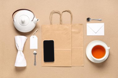 Bej arka planda cep telefonu, çay seti ve teslimat kağıtları içeren kompozisyon