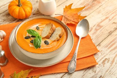 Bir kase lezzetli kabak kremalı çorba, tohumlu, kızarmış ekmek, fesleğen ve kaşık ahşap arka planda.