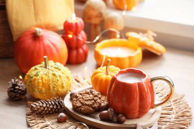 Balkabaklı latte, kurabiye, mum ve sonbahar dekoru evdeki oturma odasındaki masada.
