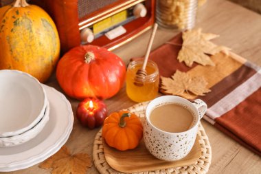 Evdeki mutfak masasının üzerinde radyo ve sonbahar dekoru olan bir fincan balkabaklı latte.