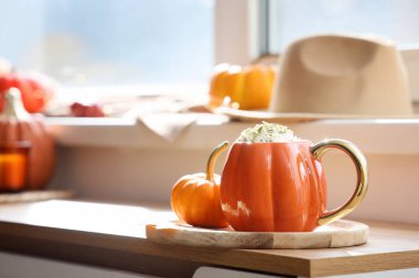 Evdeki pencerenin yanındaki masada sonbahar dekoru olan bir fincan balkabaklı latte.