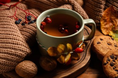 Ahşap arka planda gül kalçası çayı, kurabiye ve süveter eşliğinde kompozisyon, yakın plan