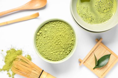 Bir kase taze kibrit çayı, toz, chasen, chashaku ve beyaz arka planda taze yapraklar.