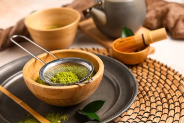 Hafif arka planda pudralanmış kibrit çay, elek, chasen ve chashaku ile kase