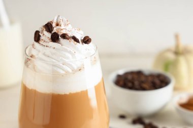 Beyaz arka planda kremalı ve kahve çekirdekli bir bardak sıcak kabaklı latte.