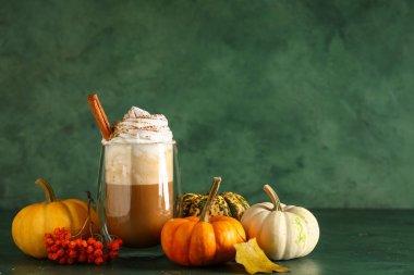 Yeşil arka planda krem şantili ve tarçınlı bir bardak sıcak kabaklı latte.