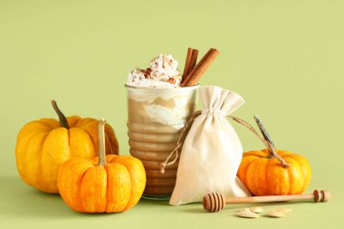 Yeşil arka planda krem şantili ve tarçınlı bir bardak sıcak kabaklı latte.