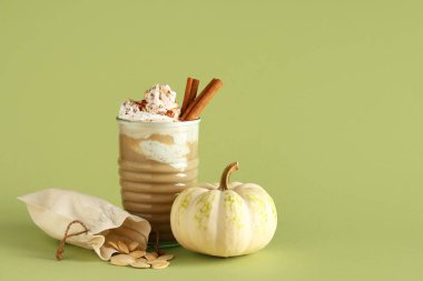 Yeşil arka planda krem şantili ve tarçınlı bir bardak sıcak kabaklı latte.