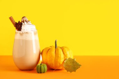 Bir bardak sıcak balkabaklı latte. Sarı arka planda krem şantili.