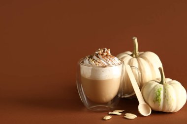 Kahverengi arka planda krem şantili ve tohumlu bir bardak sıcak kabaklı latte.