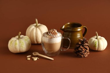 Kahverengi arka planda krem şantili ve tohumlu bir bardak sıcak kabaklı latte.