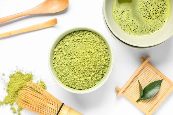 Bir kase taze kibrit çayı, toz, chasen, chashaku ve beyaz arka planda taze yapraklar.