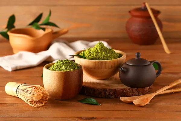 Tahta arka planda pudralanmış kibrit çayı, çaydanlık ve chasen ile kaseler