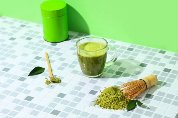 Bir fincan taze kibrit çayı, toz, chashaku, kavanoz ve yeşil duvara karşı gri fayans üzerinde chasen.