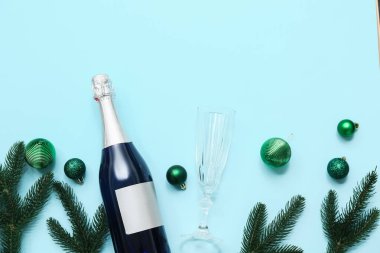 Cam kaplı bir şişe şampanya, Noel ağacı dalları ve mavi arka planda toplar.