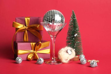 Cam, disko topları, hediye kutuları ve kırmızı arka planda Noel dekoru.