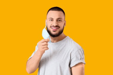 Sarı arka planda tıbbi bandı ve tıbbi maskesi olan genç bir adam.