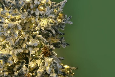 Yeşil duvarın yanında parıldayan ışıklar ve mücevherlerle süslenmiş Noel ağacı, yakın plan.