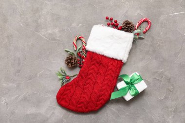 Hediyeli Noel çorabı, baston şekerler, koniler ve gri arka planda ökseotu dalları. Üst görünüm
